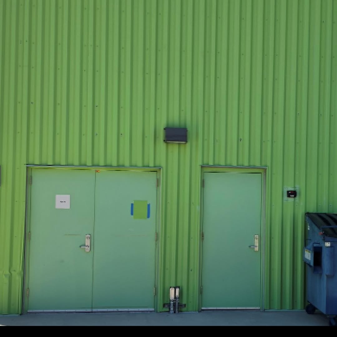 Faded green swing doors beside green metal wall panels, with a taped color standard showing the degree of fading and color drift.
